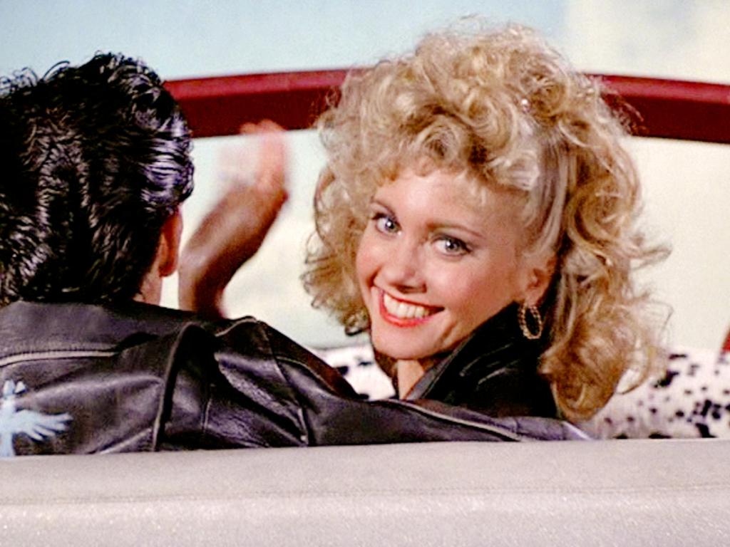 Olivia Newton-John in the final scene of the 1978 musical film, Grease, waving goodbye to the audience as she and Danny Zuko fly into the sky above. Photo Credit: Paramount Pictures